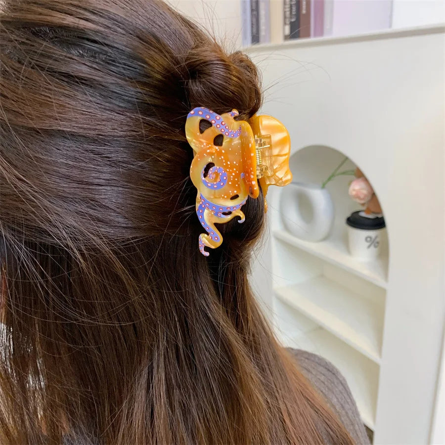 Gros plan sur les cheveux noirs d'une femme, attachés en queue de cheval avec des pinces à cheveux en forme d'octopus dorées 
