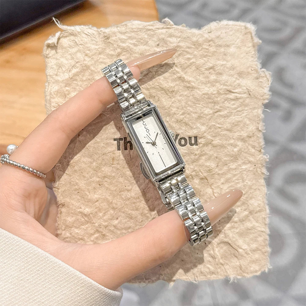 A close-up shot of a vintage gold stainless steel quartz watch worn on a finger, resting on a beige textured surface.