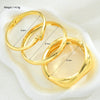 Three gold geometric wave bangles displayed in a white dish with dimension measurements.