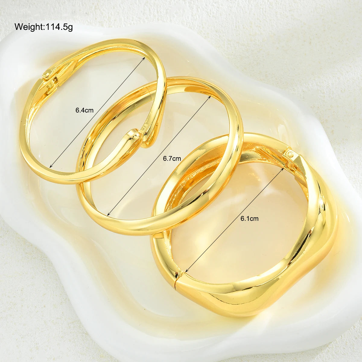 Three gold geometric wave bangles displayed in a white dish with dimension measurements.