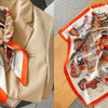 A floral print silk scarf featuring orange and white patterns is displayed on a beige blazer.