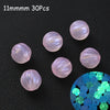 A collection of 30 iridescent pink acrylic beads scattered on a dark surface with a cluster of glowing blue beads.