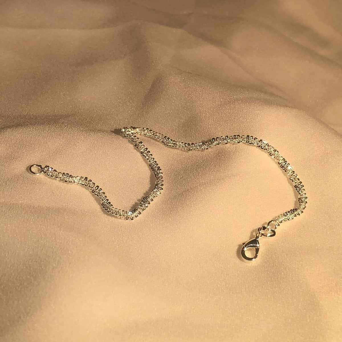 Glänzende Sterling-Silber-Halskette, die auf einem glatten beigen Stoff liegt.