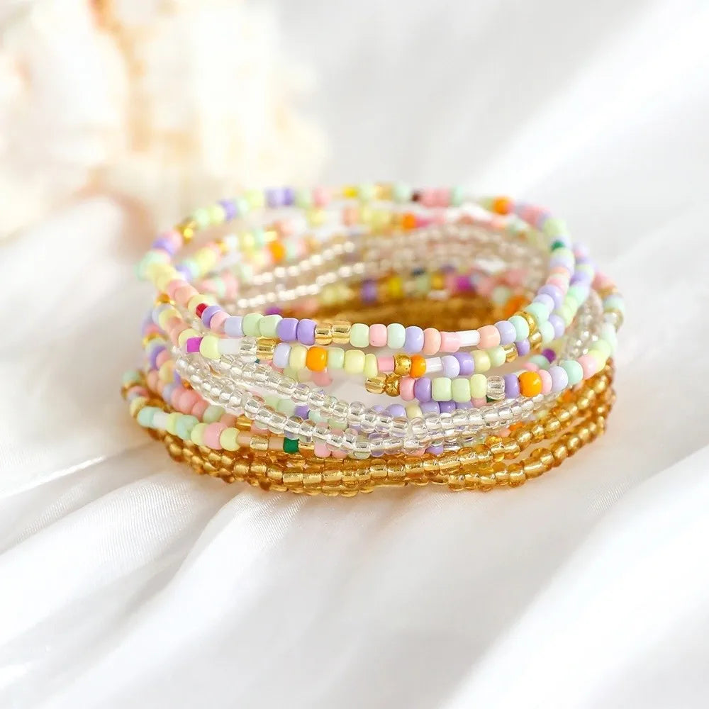 A stack of colorful beaded bangles featuring pastel pink, yellow, and purple beads on a white background.