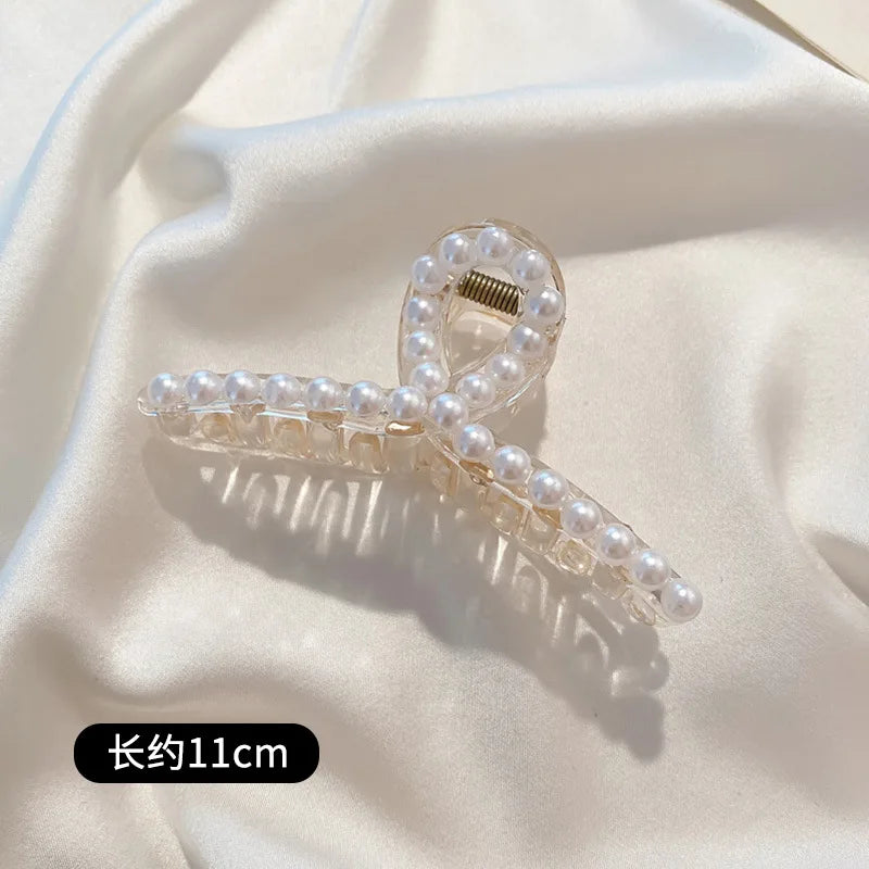 A delicate hair claw made of faux pearls, light ivory color, shown against a soft white fabric background.