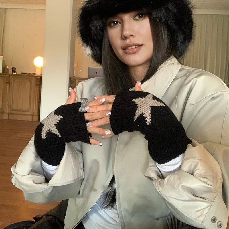 Una mujer modela guantes de punto sin dedos negros con patrones de estrellas blancas bajo una chaqueta beige claro.