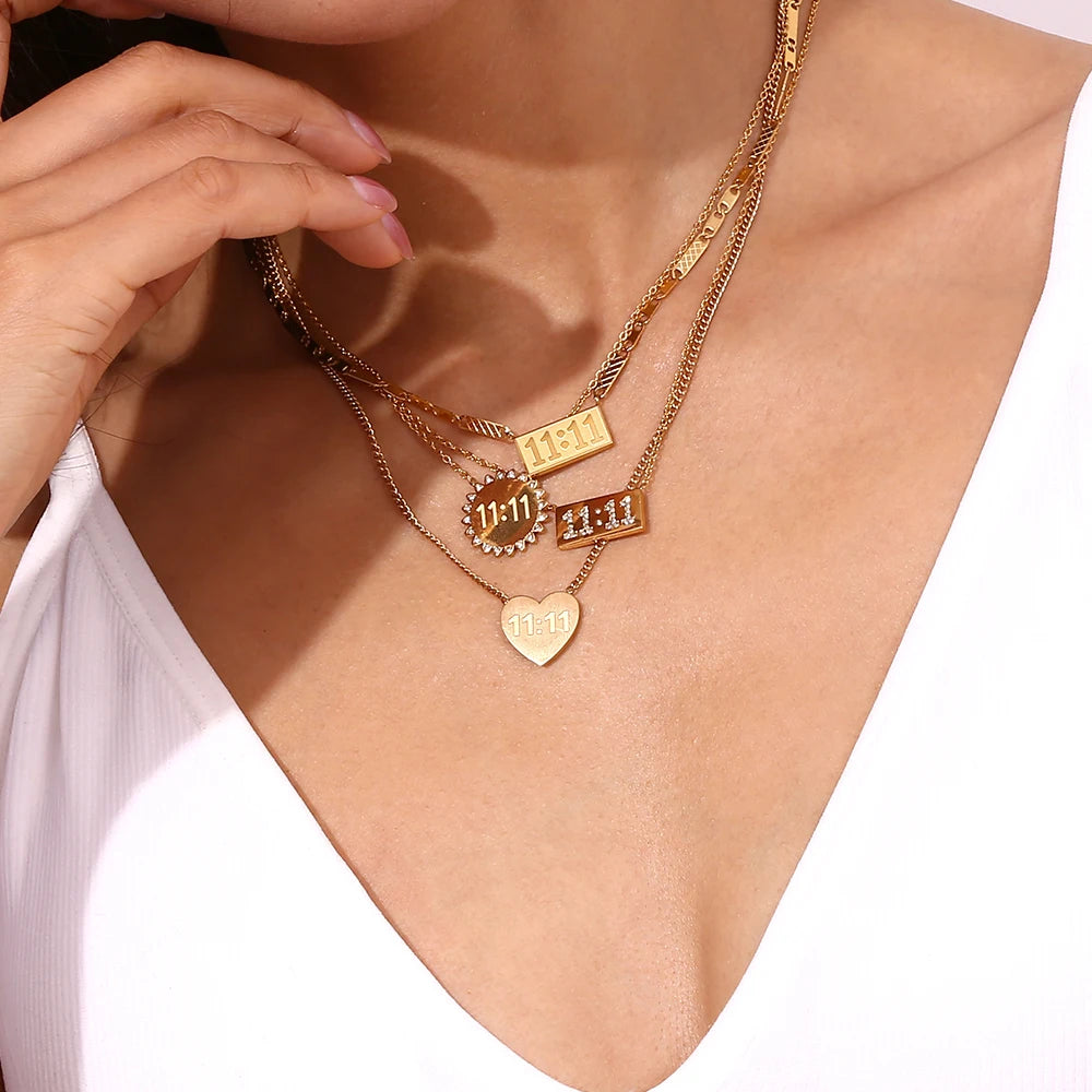 A close-up of a gold plated rectangle pendant necklace with stacked charms worn around the neck.