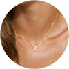 A close-up of a gold plated alphabet initial necklace resting on a person's neck and collarbone.