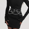 Vestido negro usado por una modelo con un cinturón arnés de cuero falso ajustable y cadenas plateadas.