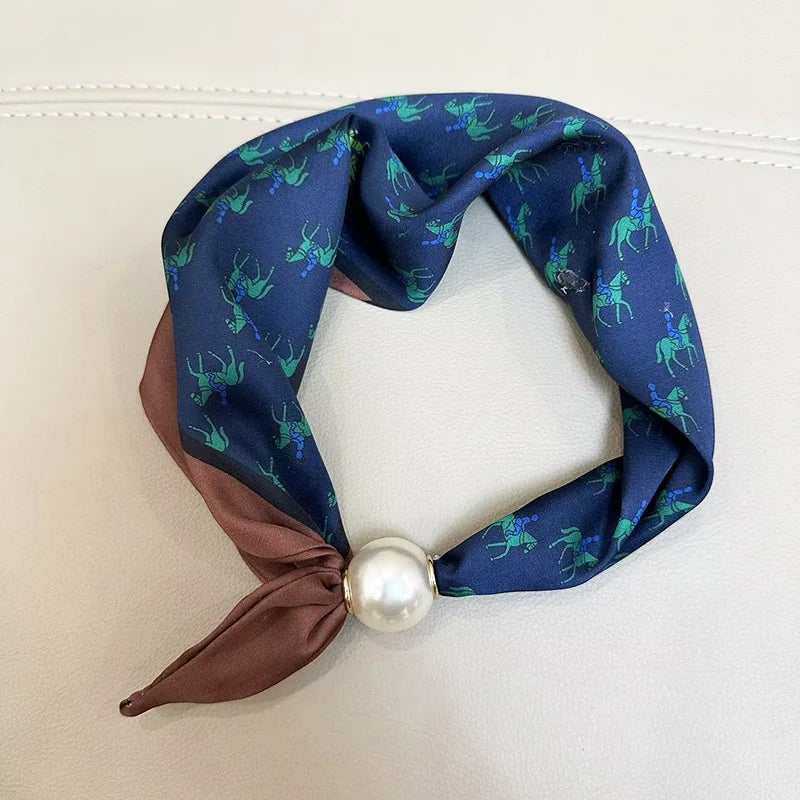 A navy blue silk scarf with a green deer print tied in a knot and secured with a pearl magnetic clasp.