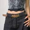 A close-up of dark denim pants and a gray floral top paired with a brown leather belt featuring bronze rivets.
