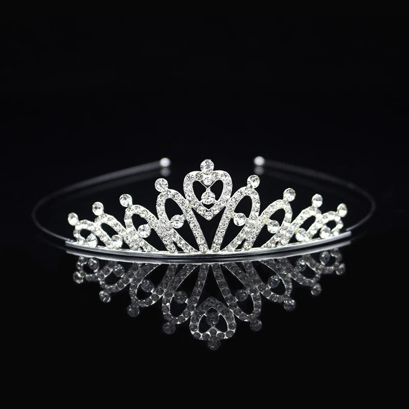 Tiara y corona de princesa de cristal brillante con accesorios para el cabello, exhibidos en una superficie reflectante.