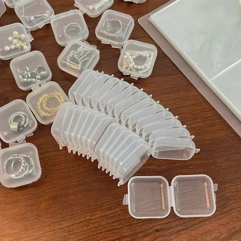 Eine Sammlung transparenter Mini-Quadrat-Aufbewahrungsboxen gefüllt mit Schmuck und Ohrringen auf einer Holzoberfläche.