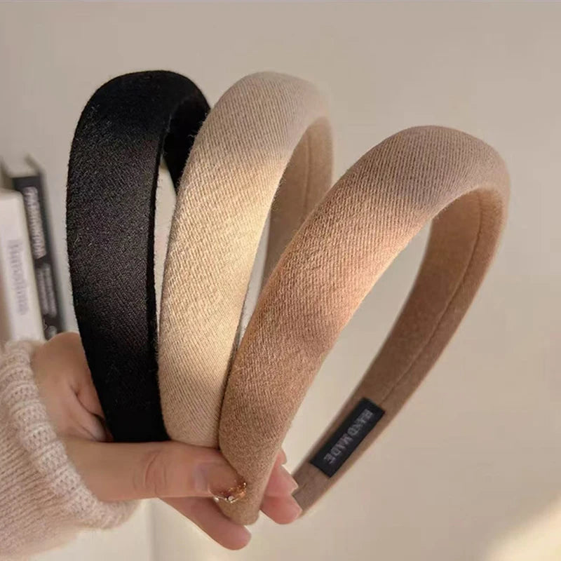 Une main tient un bandeau pour cheveux épaissi de couleur café avec des options noir et beige.