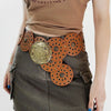 A close-up of a brown top and dark green skirt featuring multiple vintage PU disc belts with metal buckles.
