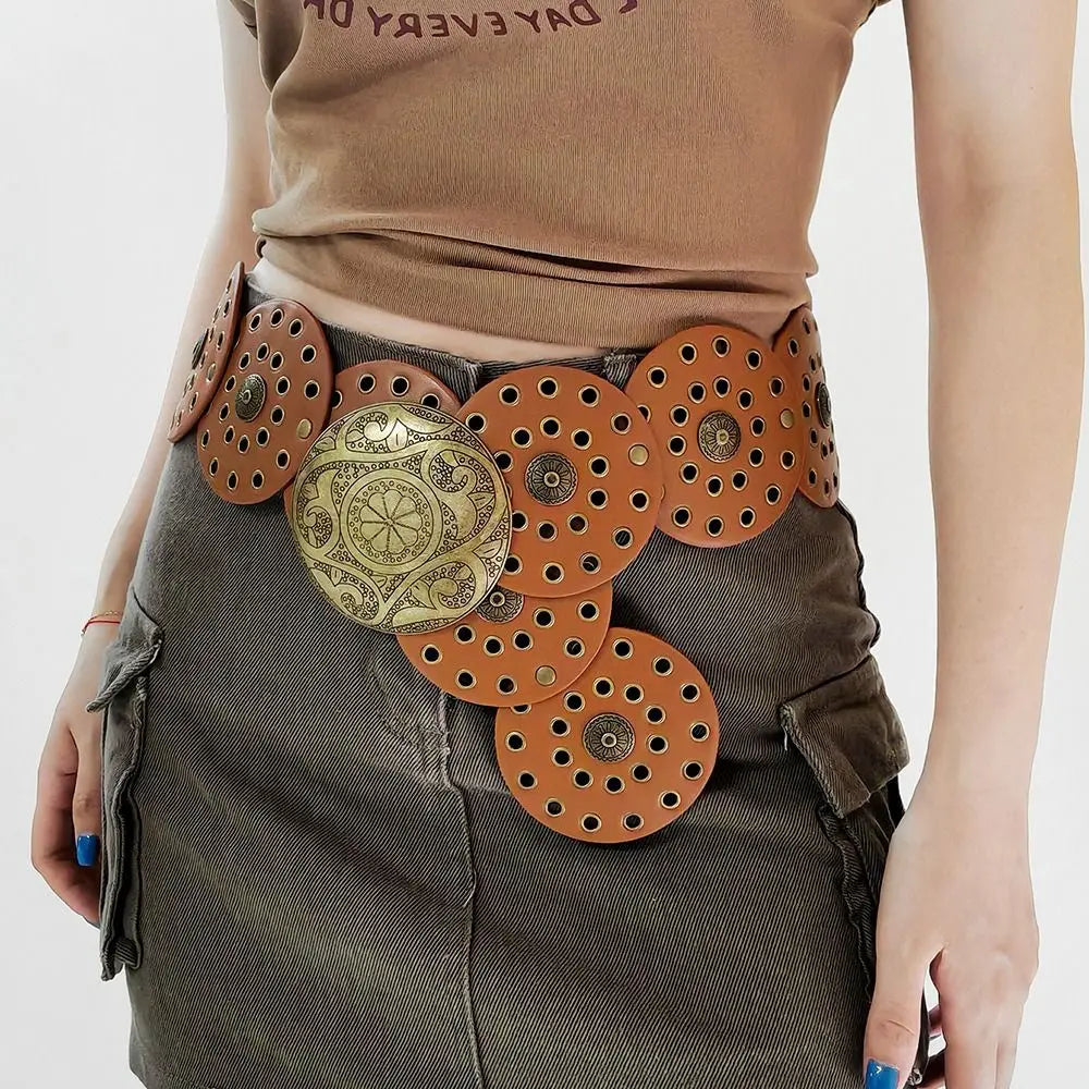 A close-up of a brown top and dark green skirt featuring multiple vintage PU disc belts with metal buckles.