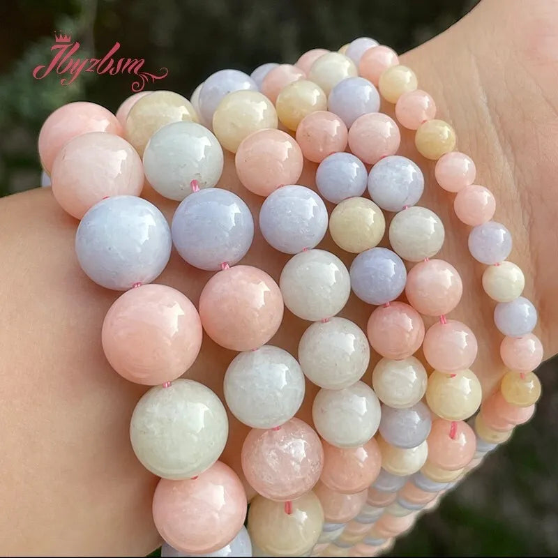 A hand is holding a string of smooth round jade beads in various shades of pink, white, and lavender.