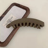 A set of large banana hair clips in a matte olive green color resting on a wooden tray with a white cloth.