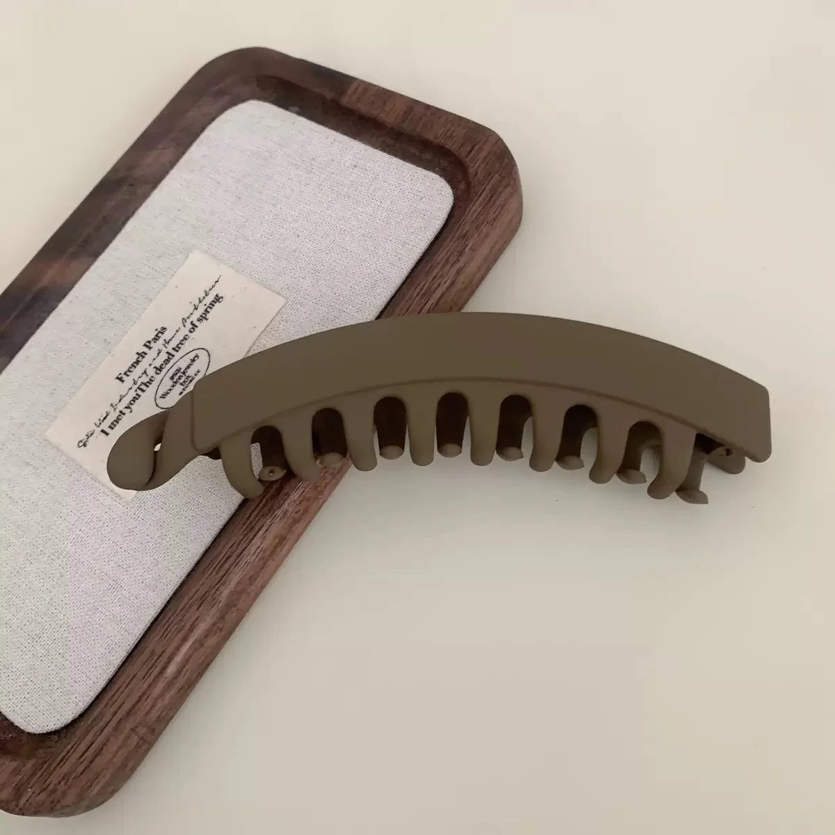 A set of large banana hair clips in a matte olive green color resting on a wooden tray with a white cloth.