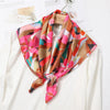A flowing silk scarf in shades of pink, coral, and brown is tied around a white blouse.