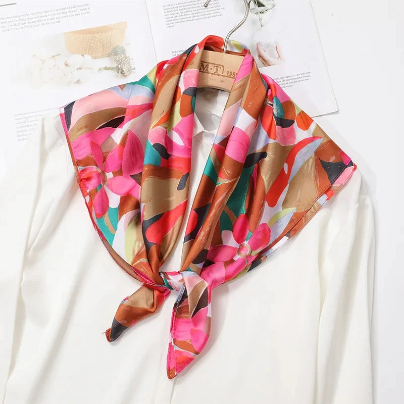 A flowing silk scarf in shades of pink, coral, and brown is tied around a white blouse.