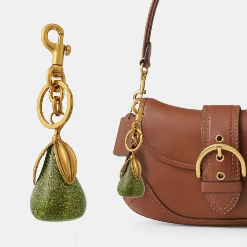 Charm en forme de poire vert cristal attaché à une clé USB dorée sur un sac en cuir marron.