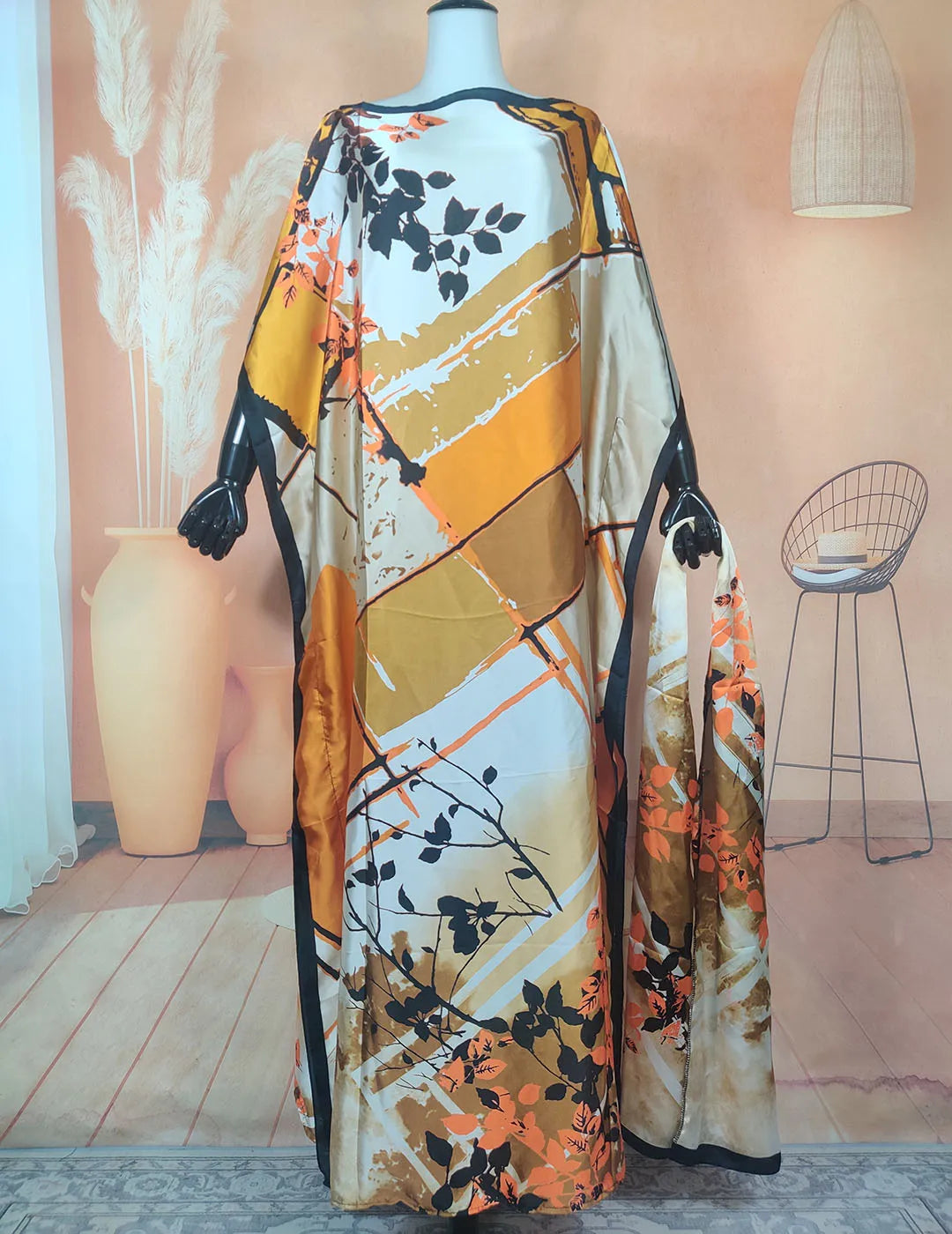 A long, flowing kaftan dress in beige and orange floral print displayed on a mannequin.