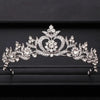 A sparkling crystal bridal crown with intricate floral and heart designs displayed on a dark background.