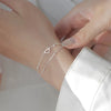 A close-up of a sterling silver double heart charm bracelet worn on a slender wrist.