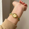 Gros plan d'une montre-bracelet dorée avec des accents de jade vert portée au poignet.