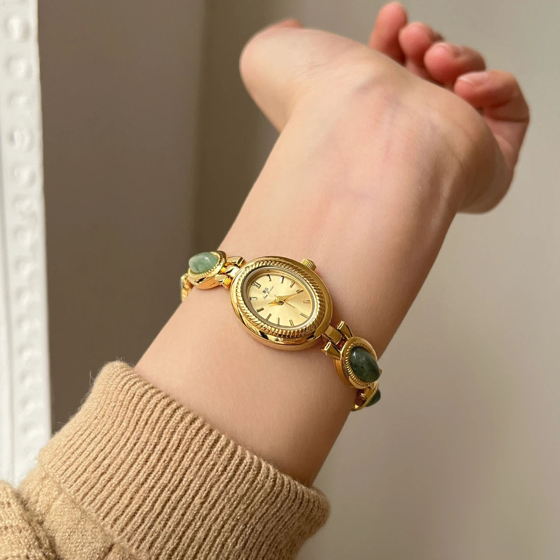 Gros plan d'une montre-bracelet dorée avec des accents de jade vert portée au poignet.