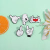A collection of white enamel pins depicting various cartoon finger gestures, including a thumbs up and a heart sign.
