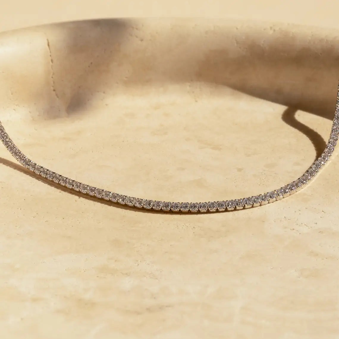 Primer plano de un collar choker con circonitas de hielo sobre una superficie beige claro.