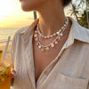 A close-up of a woman wearing a delicate boho shell starfish necklace against a sunset beach background.