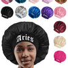 A woman wearing a black satin sleep bonnet with an Aries wrap band, surrounded by various colored satin bonnets.