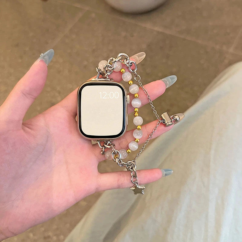 A hand holds a square digital watch with a clear face and a delicate double chain watch strap made of light pink beads.