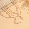 A delicate gold layered necklace featuring small pearls and a cross pendant displayed on a neutral background.