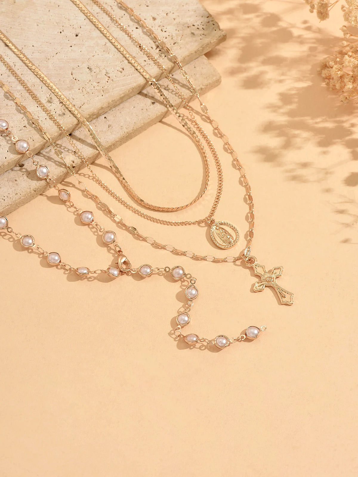 A delicate gold layered necklace featuring small pearls and a cross pendant displayed on a neutral background.