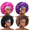 A set of three satin sleep bonnets in pink, purple, and black with elastic bands shown on a model's head.