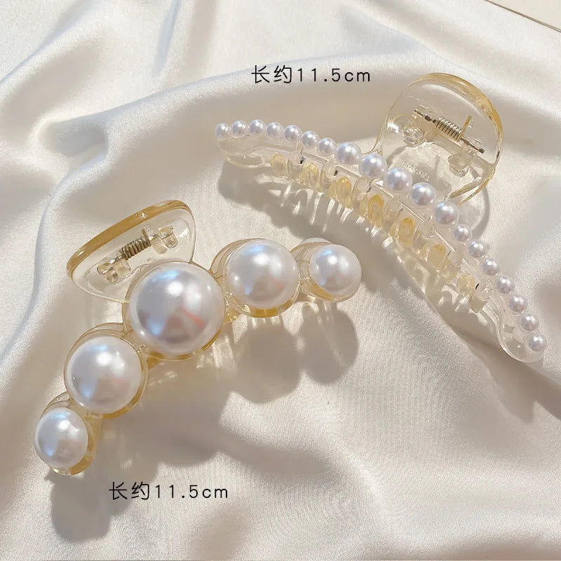 Clear acrylic hair claws with faux pearls, shown against a white fabric background.