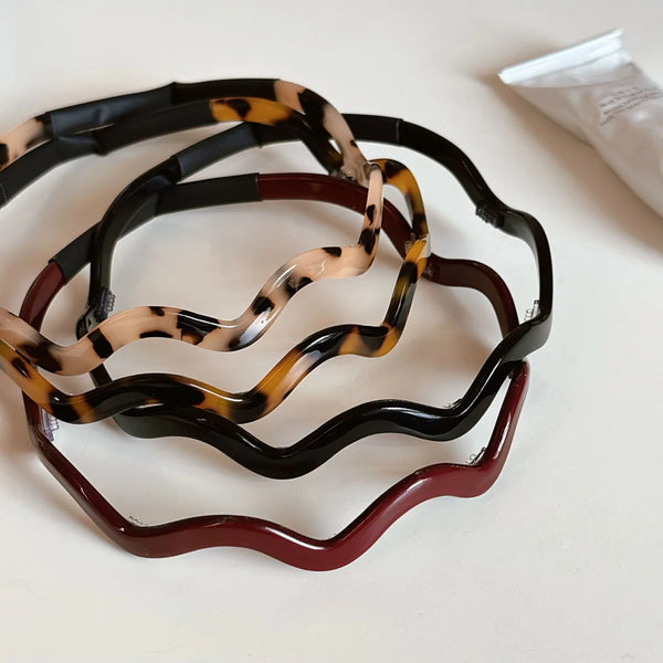 A set of retro tortoiseshell wavy acetate hair hoops in black, brown, and reddish-brown.