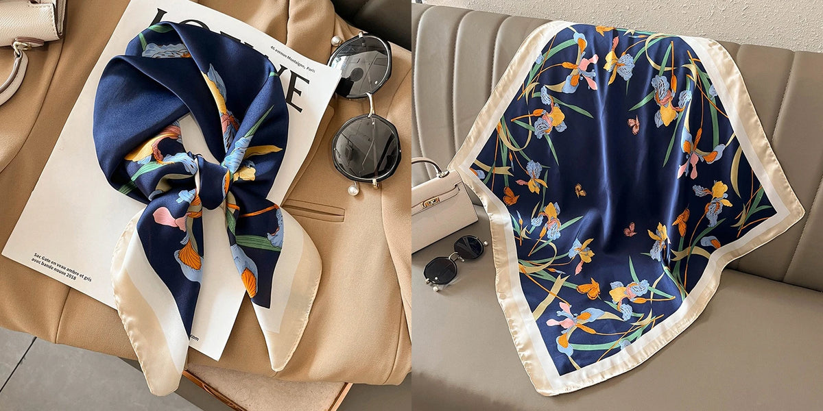 A navy blue silk scarf with a floral print featuring orange and blue flowers is displayed on a beige fabric.