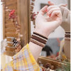 A hand wearing a stacked brown and beige beaded bracelet is visible next to some natural elements.