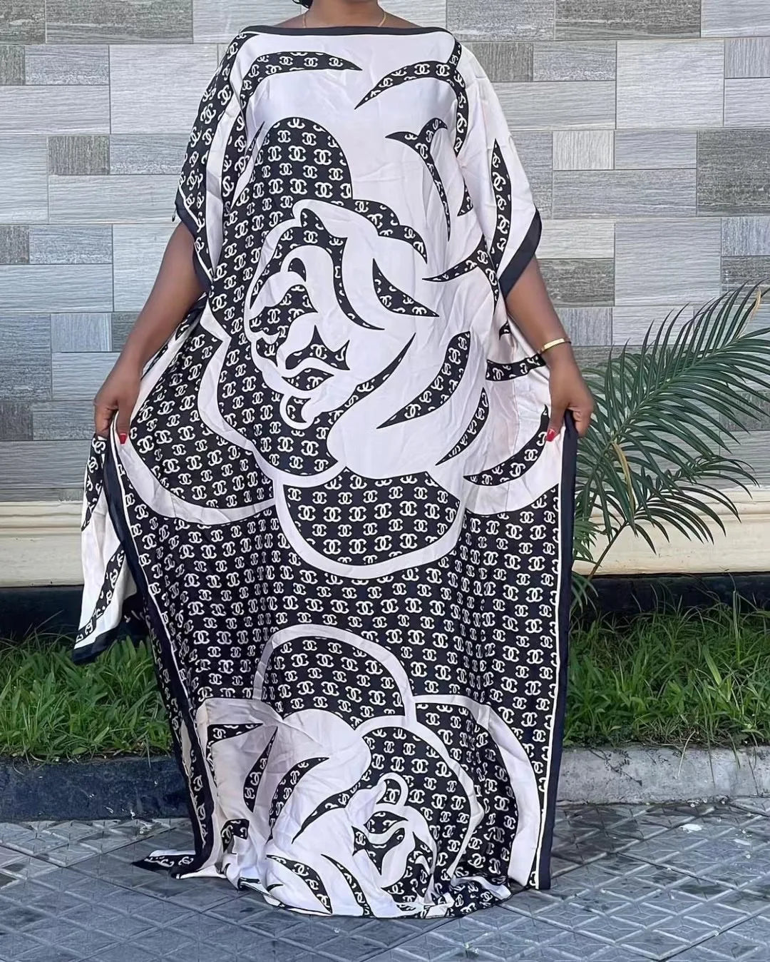 Eine Frau in einem schwarz-weißen gemusterten Kaftankleid mit schwarzem Zierrand, draußen stehend.