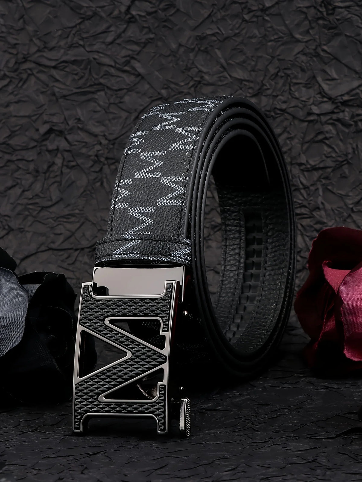 Cinturón de moda estampado negro con hebilla plateada, mostrado contra un fondo oscuro y texturizado.