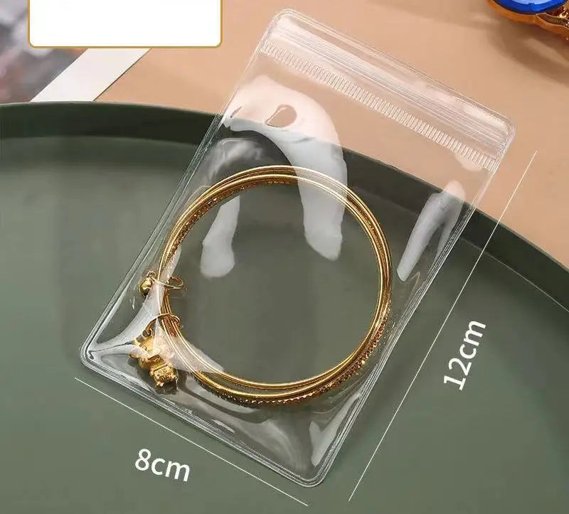 A clear self-sealing jewelry storage pouch containing a gold-colored ring, shown on a green plate.