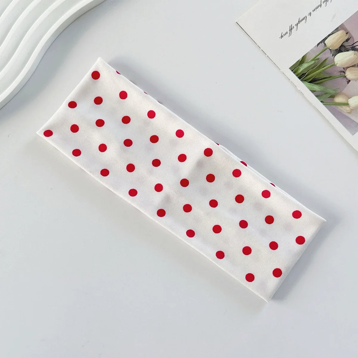 A white fabric headband with red polka dots is displayed on a light surface.