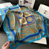 A bright turquoise silk scarf with intricate gold and blue floral patterns is displayed on a dark surface.
