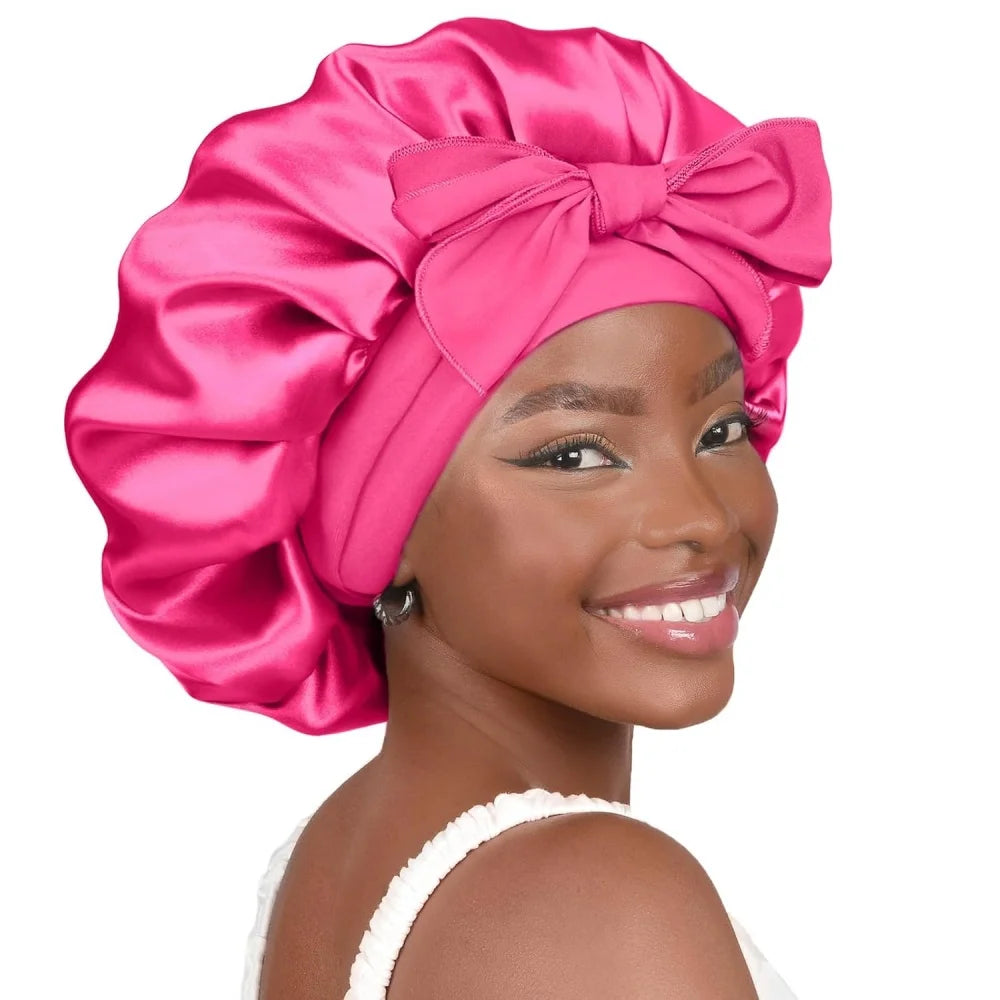 A woman models a vibrant pink satin sleeping bonnet tied in a bow.