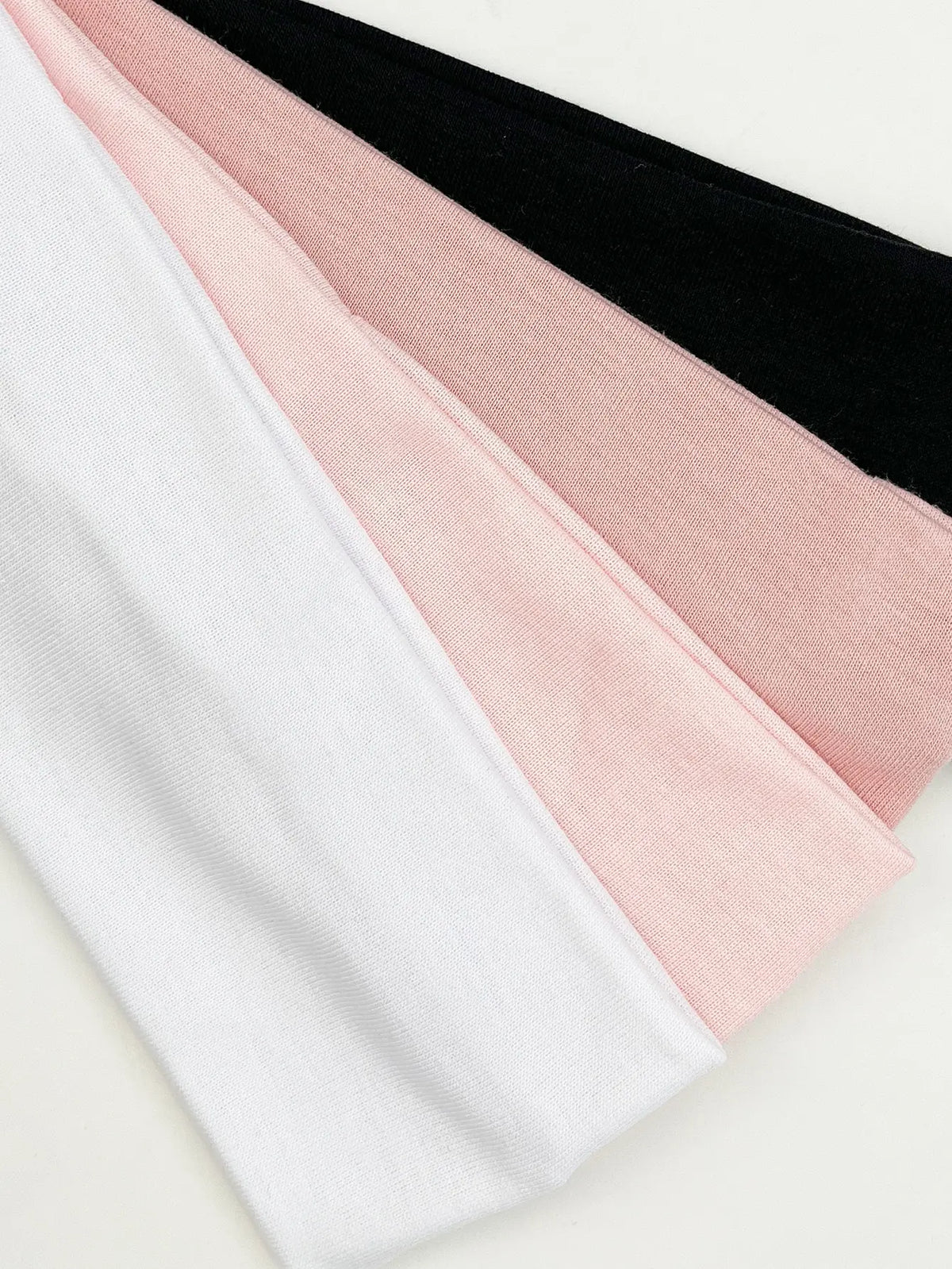 A stack of four knitted hair bands in white, pink, and black colors.